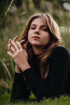 a woman is sitting in the grass with her hands on her chest and looking off into the distance