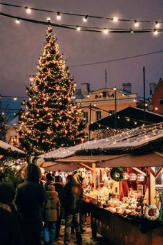 a christmas tree is lit up in the background as people walk by at an outdoor market