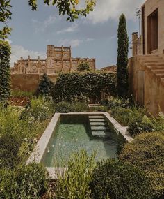 an outdoor swimming pool surrounded by greenery and stone steps in front of a castle like building