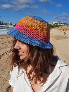 a woman wearing a multicolored crocheted hat on top of a sandy beach