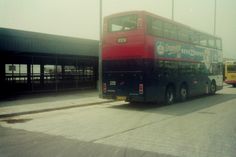 a red and black double decker bus parked in front of a building with two other buses