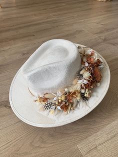 Introducing this handcrafted fedora with an intricate floral embroidery, a unique and stylish handmade hat that will elevate your fashion game to the next level. Made with high-quality materials and great attention to detail, this wide brim fedora hat is designed to provide you with comfort, style, and durability.   Highlights:  - Handmade with great attention to detail  - Features a multicolor dried floral crown tied band - Comes in a classic white color that can easily pair             with an Elegant Cream Luxury Fedora, White Wide Brim Festival Hat, White Wide Brim Costume Hat For Festival, White Brimmed Fedora For Festival, White Fedora With Short Brim For Festivals, White Short Brim Fedora For Festival, White Bohemian Fedora Felt Hat, Bohemian White Fedora Felt Hat, White Curved Brim Fedora For Festival