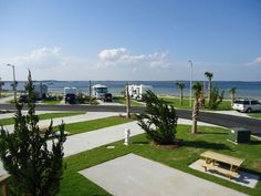 an rv park near the ocean with cars parked on the grass and trees in front of it