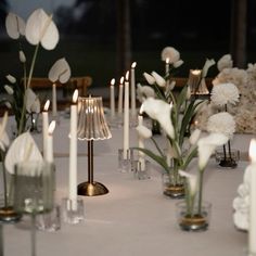 the table is set with candles and flowers in glass vases, which are also filled with white carnations