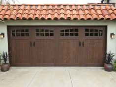 two large brown garage doors in front of a stucco building with potted plants on the side