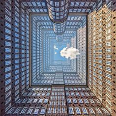 the view from below looking up into a building with many windows and a cloud in the sky