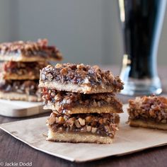 three pieces of pecan bar sitting on top of a piece of parchment paper next to a glass of beer