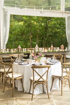 a table set up with white linens and place settings for an outdoor dinner party