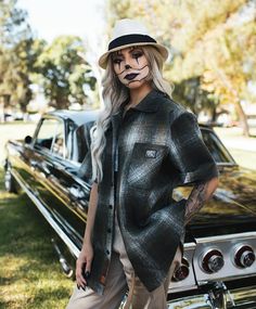 a woman with makeup painted on her face standing next to a black and white car