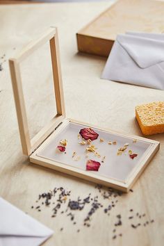 an open wooden box with dried flowers in it on a table next to a piece of bread