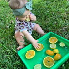 a baby sitting in the grass with lemons and oranges on it's tray