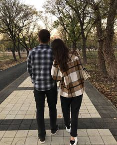 a man and woman walking down a sidewalk in the fall with trees lining the walkway