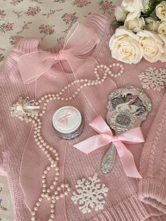 a pink sweater with pearls and flowers on the table next to it is a jar of perfume