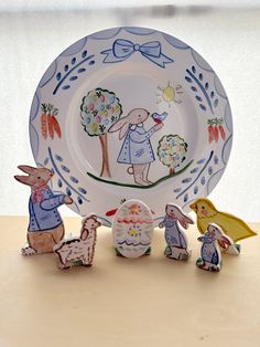 three small figurines in front of a plate with an image of rabbits on it