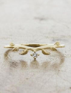 a yellow gold ring with leaves and a diamond on the top, sitting on a table