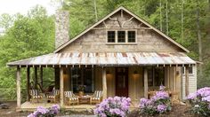 a small wooden cabin in the woods with flowers on the front lawn and patio area