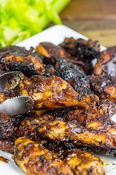 a white plate topped with chicken wings covered in bbq sauce next to lettuce