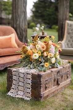 an old trunk with flowers in it sitting on the grass next to a couch and chair