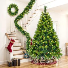 a christmas tree in the middle of a room next to a stair case with stockings on it