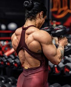 a woman in a gym holding two dumbs and looking at the back of her body