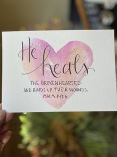 a person holding up a card with the words he heals and a heart painted on it