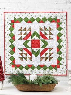 a green and red christmas quilt hanging on a wall next to a potted plant