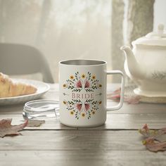 a white coffee mug sitting on top of a wooden table next to a tea pot