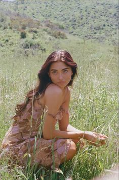 a young woman sitting in the grass with her hands on her knees and looking at the camera