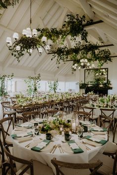 tables and chairs are set up for an event with greenery hanging from the ceiling