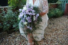 a woman in a white dress holding a bouquet of purple and white flowers on her wedding day