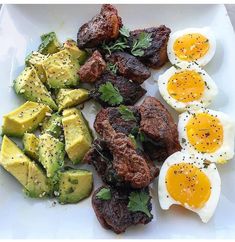 a white plate topped with meat, eggs and avocado on top of it