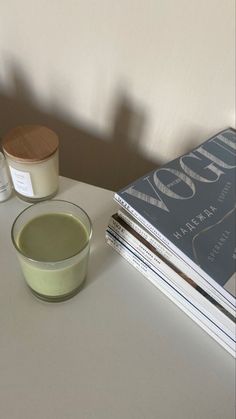 a white table topped with books and a bowl of green liquid next to a candle