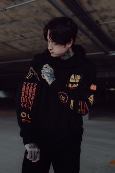 a man with tattoos wearing a black hoodie and standing in an empty parking lot