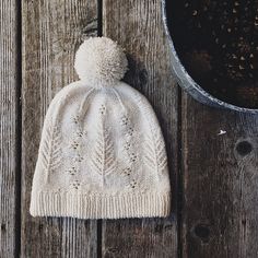 a white knitted hat sitting on top of a wooden table next to a potted plant