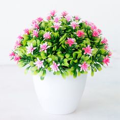 a white vase filled with pink flowers on top of a table