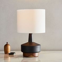 a table lamp sitting on top of a white counter next to a brown vase and a wooden container