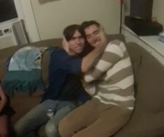 two people sitting on a couch with their arms around each other and one person taking a selfie