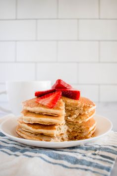 a stack of pancakes with strawberries on top and a cup of coffee in the background