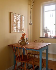 a dining room table with two chairs and a vase on top of it next to a window