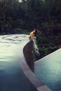 a woman sitting in the middle of a pool with trees behind her and water running down it