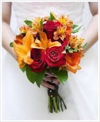 a bridal bouquet with orange, red and yellow flowers is held by a bride