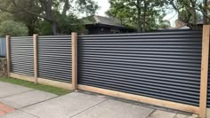 a black metal fence with wooden posts on the side of a sidewalk in front of a house