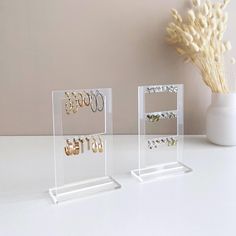 two clear acrylic displays with earrings on them and a vase full of flowers