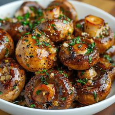 a white bowl filled with cooked mushrooms covered in sauce and garnished with parsley