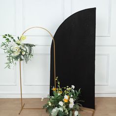 an arrangement of flowers and greenery on a stand in front of a white wall