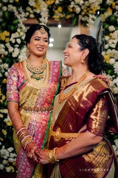 two women standing next to each other in front of flowers