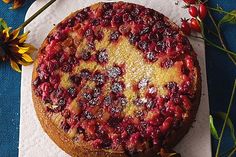 a cake with berries on it sitting on top of a paper towel next to flowers