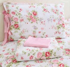 a bed topped with lots of pink flowers next to a white headboard and pillows