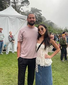 a man and woman standing next to each other in front of a white tent at an outdoor event