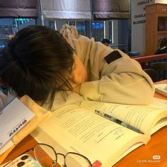 a person leaning their head on an open book while sitting at a table with other books